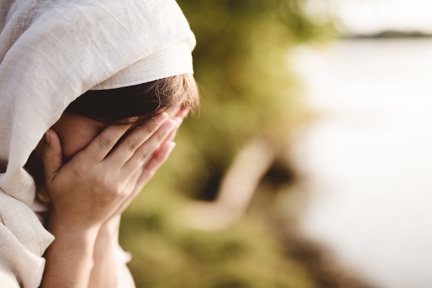 Closeup shot of a female wearing a biblical robe praying with a blurred background