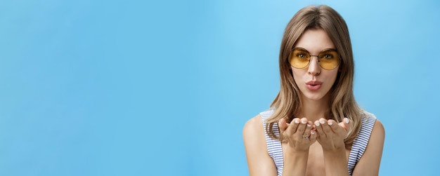 Free photo closeup shot of feminine and tender charming woman in trendy yellow sunglasses folding lips holding