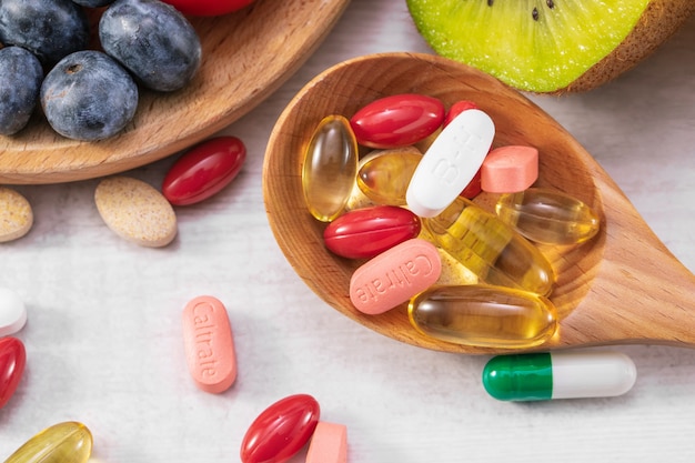 Closeup shot of fresh fruits with different medicine on a wooden spoon