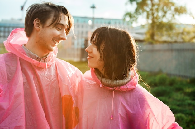 Free photo closeup shot of a male and a female in pink plastic raincoats looking at each other romantically