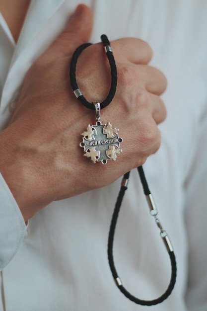 Free photo closeup shot of a male holding a charm necklace with a silver pendant and a black cord