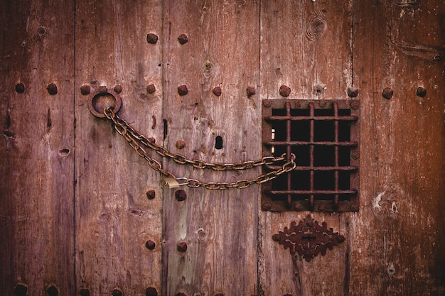 Free Photo closeup shot of an old rusty chain lock on a large wooden door with a small metal fence