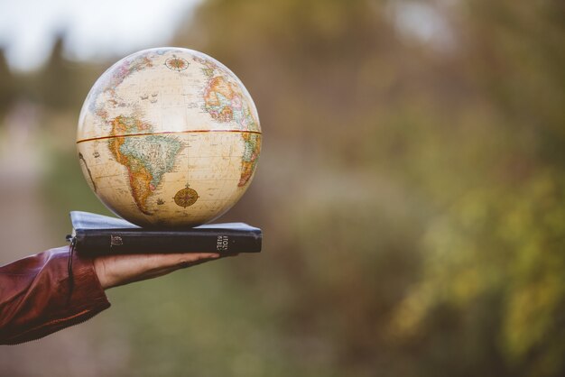 Closeup shot of a person holding bible with desk globe on top