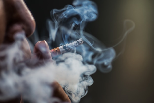 Closeup shot of a person puffing on a cigarette surrounded with smoke