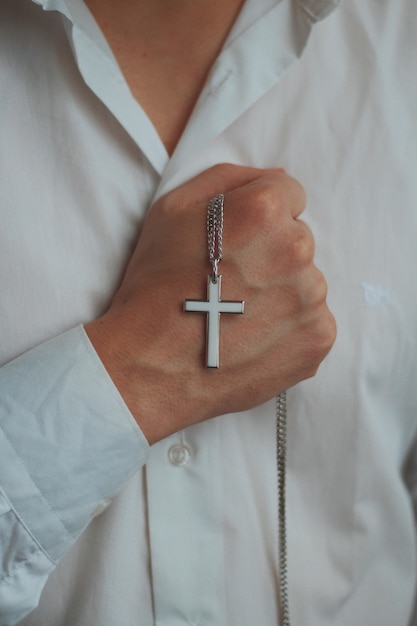 Free photo closeup shot of a religious male holding a silver necklace with a cross pendant