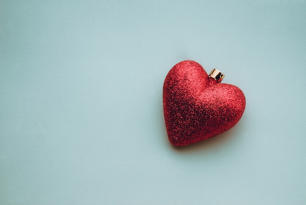 Closeup shot of shiny heart-shaped Christmas tree decoration on a light blue surface