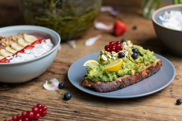 Closeup shot of a slice of brown bread with avocado pasta and a smoothie bowl