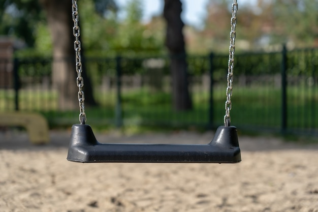 Closeup shot of a swing in front of a metal fence and trees