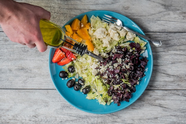 Closeup shot of a vegetable and fruit salad with a person pouring vegetable oil on it