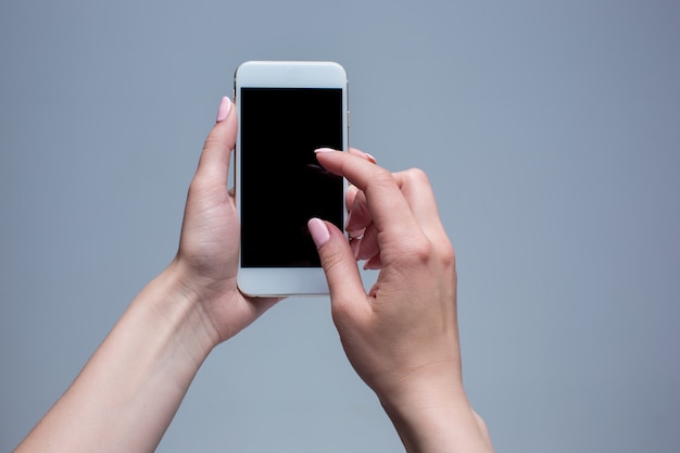 Closeup shot of a woman typing on mobile phone on gray background. Female hands holding a modern smartphone and pointing with finger.