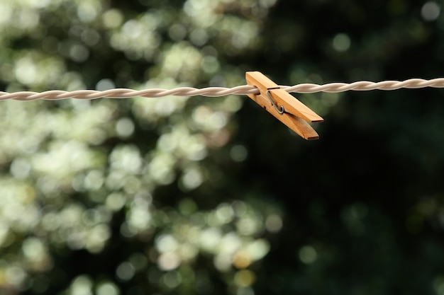 A closeup shot of a wooden clothespin on a wire with a blurred natural background