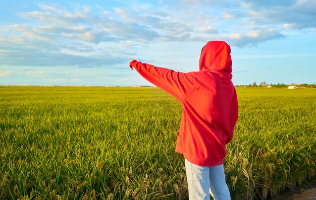 Closeup shot of a young lady in red  cheerfully standing in a  green field on a sunny day