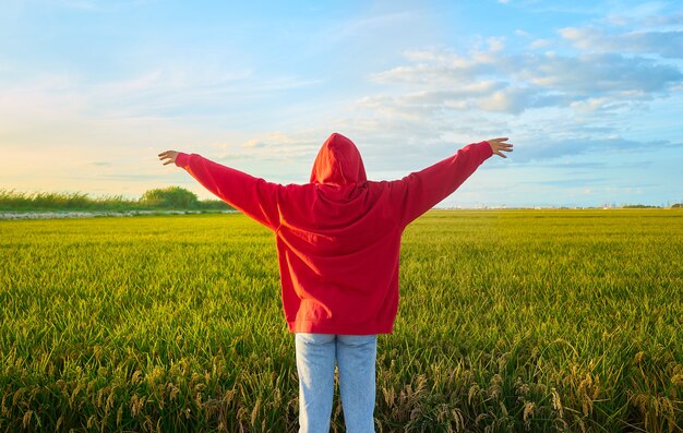 Closeup shot of a young lady in red  cheerfully standing in a  green field on a sunny day