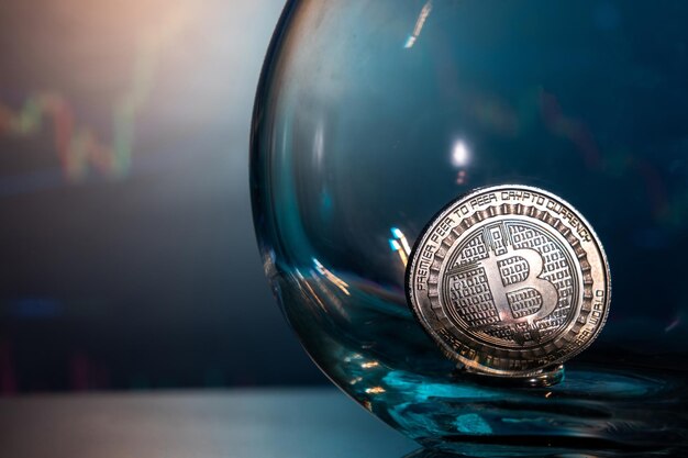 Closeup of a silver Bitcoin on a blue reflective surface in a glass and the histogram of currency