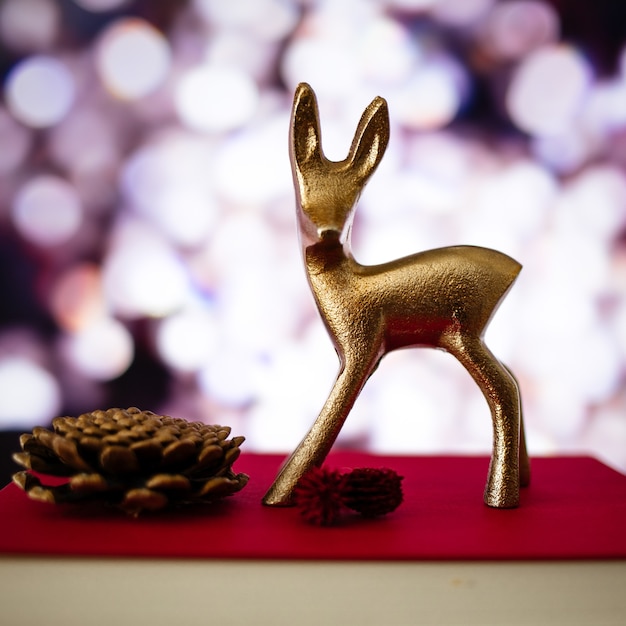 Closeup of a small deer figure and a pine cone on a book with a blurry background and bokeh lights