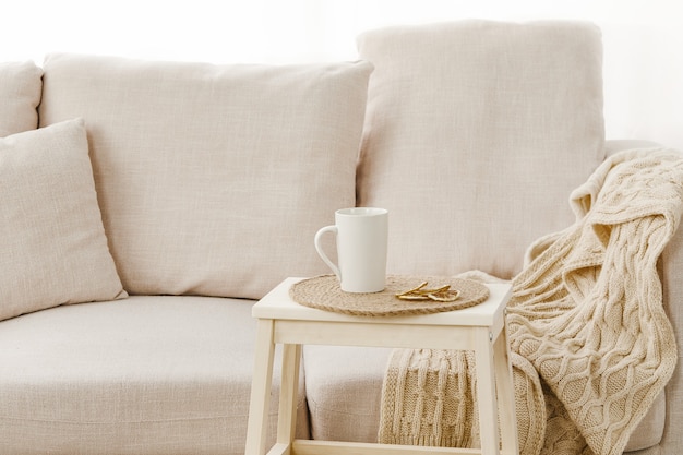 Closeup of a small table with a mug on it near a beige sofa under the lights