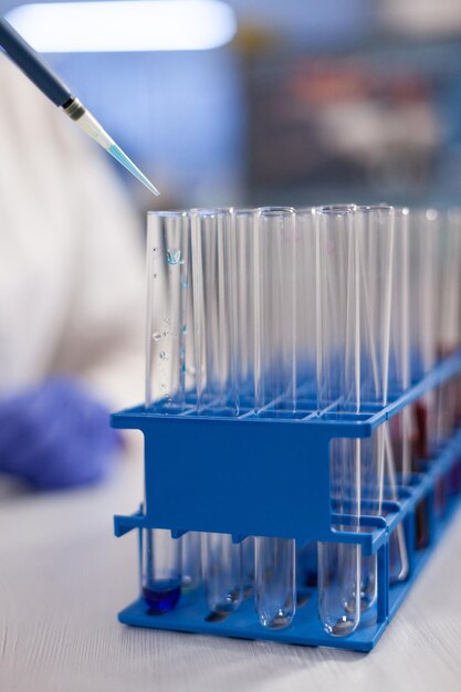 Closeup of specialist researcher putting solution in transparent test tubes working at vaccine development during microbiological experiment. Microbiology laboratory with medical equipment