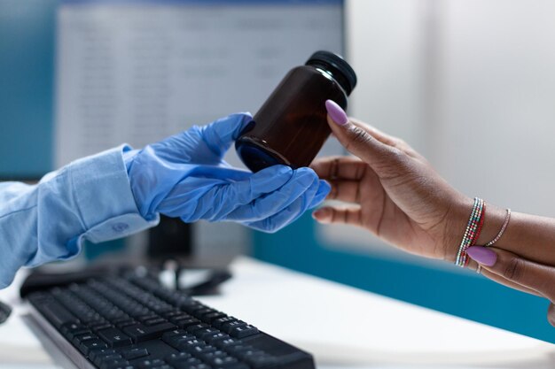 Closeup of therapist doctor hand giving pills bottle to african american sick patient discussing medication treatment during clinical appointment. Physician woman working in hospital office