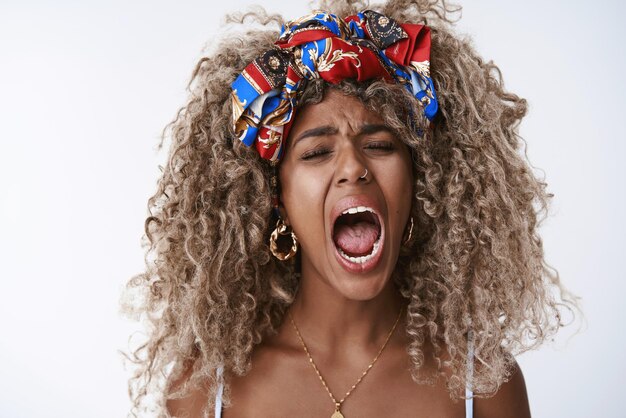 Closeup tired sleepy attractive africanamerican blond curly woman afro hairstyle in stylish hipster headband piercing yawning with closed eyes from fatigue wanna sleep hate mondays