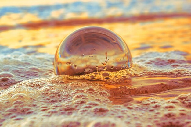 Closeup of a transparent ball on the sand surrounded by the sea during the sunset in the evening