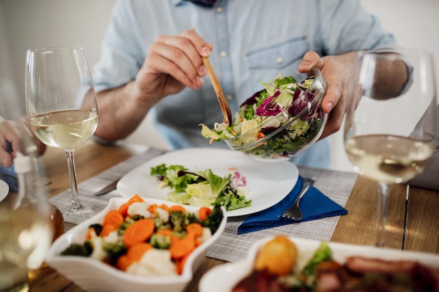 Closeup of unrecognizable man pouring salad in a plate while eating lunch at dining table