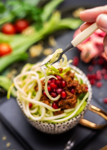 Closeup of a vegan meal with spiralized zucchini, tomato sauce and pomegranates in the cup