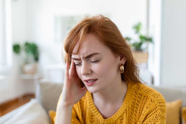 Closeup view frown face of woman feeling strong headache touch temple to reduce severe pain suffering from panic attack in office migraine overworked person or hangover alcohol abuse concept