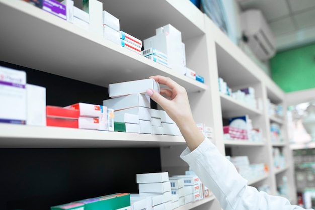 Closeup view of pharmacist hand taking medicine box from the shelf in drug store