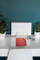 Free photo closeup view of a white desk with white papers, red notebook, plants, pen and glasses in it