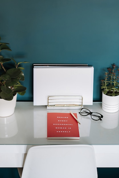 Free Photo closeup view of a white desk with white papers, red notebook, plants, pen and glasses in it