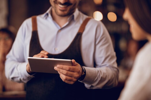 Closeup of waiter taking order on touchpad while talking to a guest in a pub