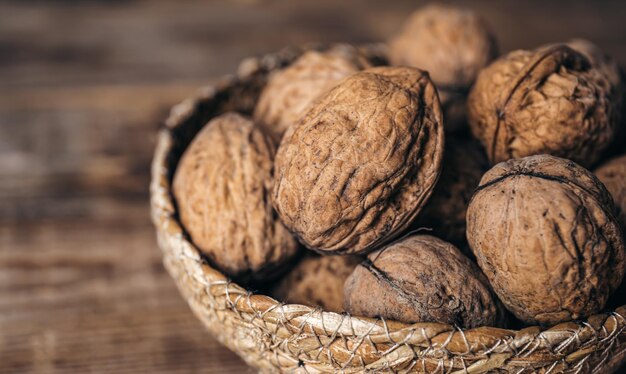 Closeup whole walnuts in a wicker bowl on a wooden background