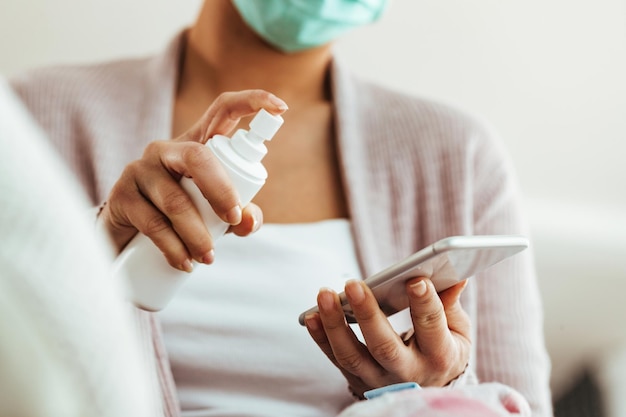 Closeup of woman using using spray bottle while cleaning her mobile phone at home