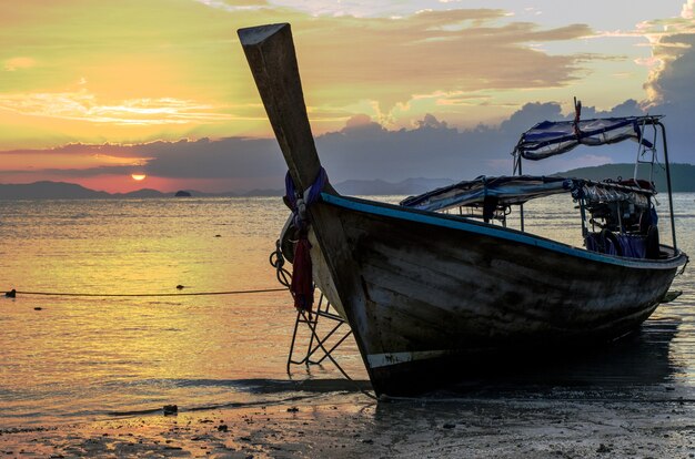 Closeup of a wooden boat on the beach surrounded by the sea under a cloudy sky during the sunset