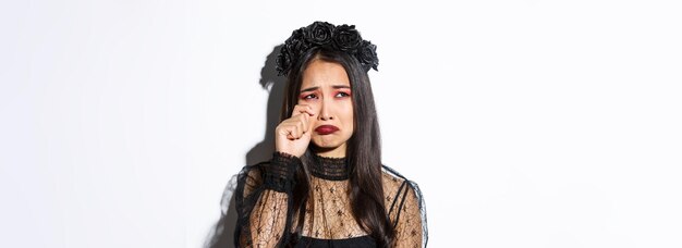 Closeup of young asian woman in witch costume crying and looking miserable feeling sad standing over