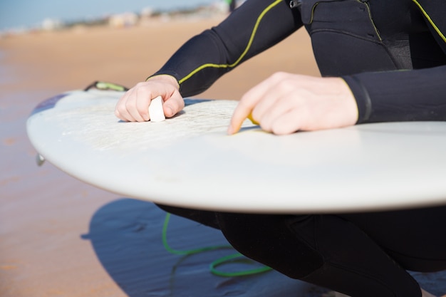 Free photo closeup of young man waxing surfboard on sunny beach