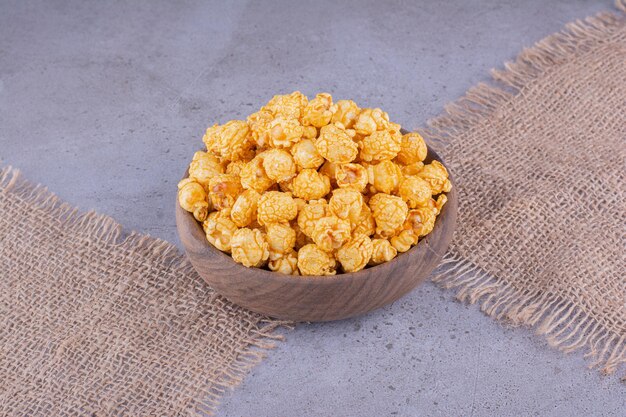 Cloth pieces underneath a wooden bowl filled with flavored popcorn on marble background. High quality photo