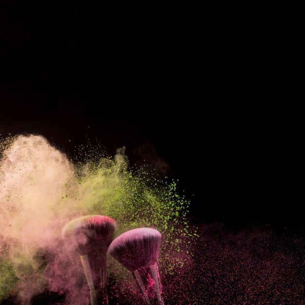 Cloud of powder and two makeup brushes at bottom on dark background