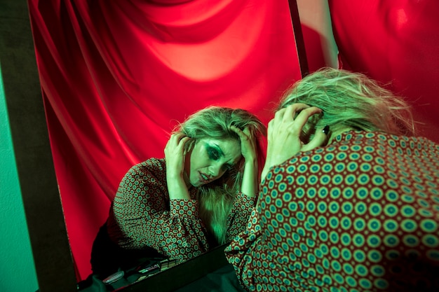 Free photo clown girl being upset in front of the mirror