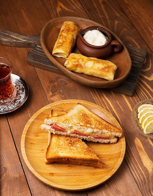 Free Photo club sandwiches with salami, bacon and blinchik served with yogurt in wooden plate with tea.