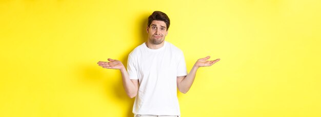 Clueless man in white tshirt shrugging and looking puzzled dont know anything standing over yellow b