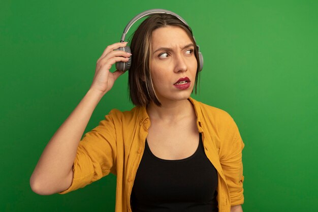 Clueless pretty caucasian woman on headphones looks at side on green