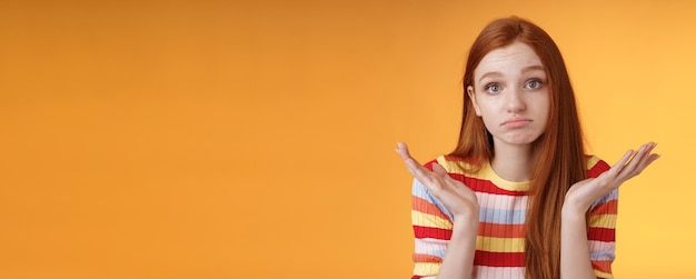 Free photo clueless upset redhead young cute female coworker shrugging hands spread sideays unaware pouting confused cannot answer question apologizing not knowing standing orange background