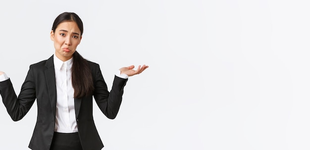 Clueless upset young asian female office worker manager in black suit shrugging with hands spread si