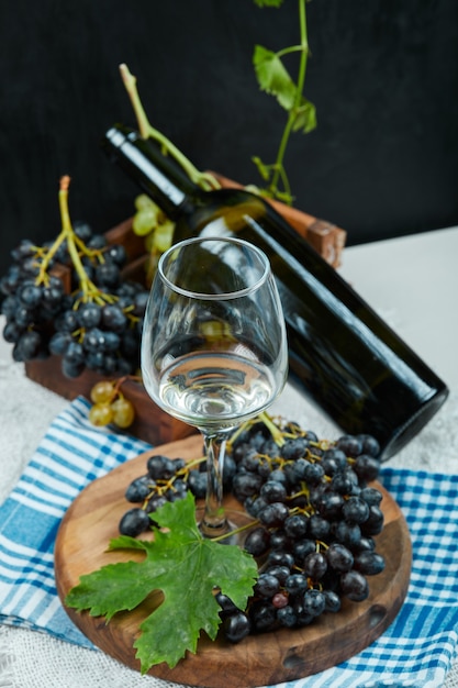 A cluster of grapes with a glass of wine and a bottle on white table with blue tablecloth. High quality photo