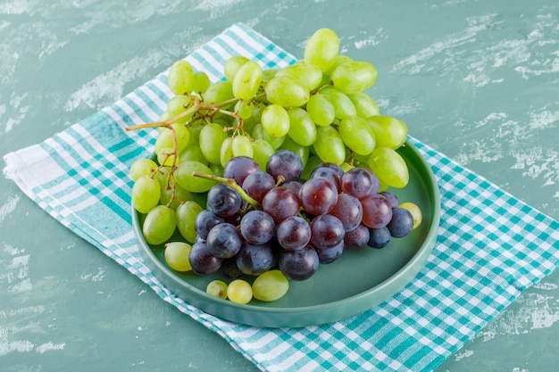 Clusters of grapes in a tray high angle view on plaster and picnic cloth background