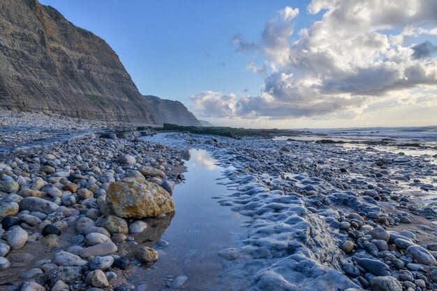 Coast surrounded by the sea and cliffs under a cloudy sky during the sunrise