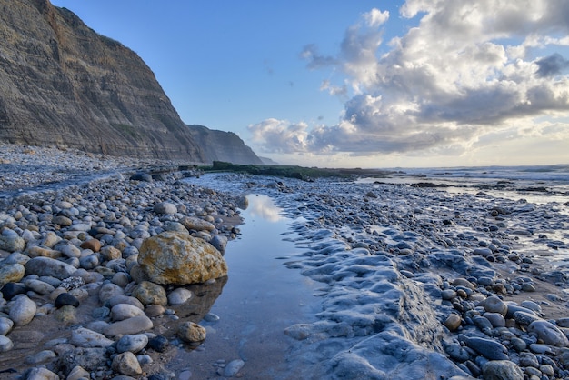 Coast surrounded by the sea and cliffs under a cloudy sky during the sunrise