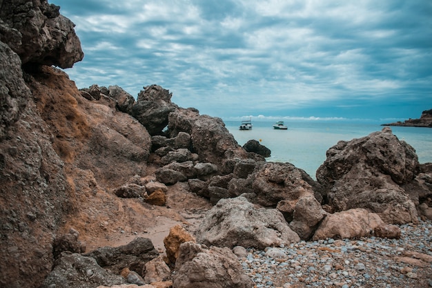 Free Photo coastline full of rocks, some ships in the sea and the cloudy sky