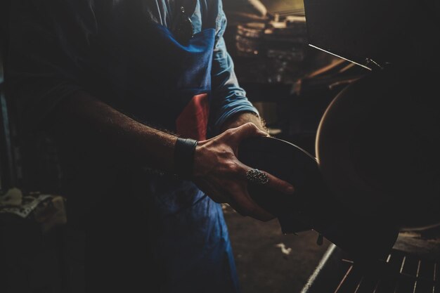 Cobbler in apron is working on shoe using special machine at his workshop.